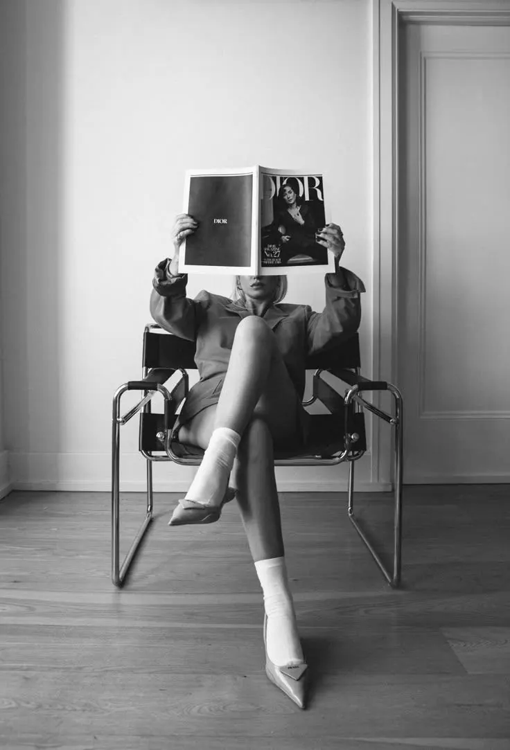 Editorial portrait of a woman seated, holding a Dior magazine